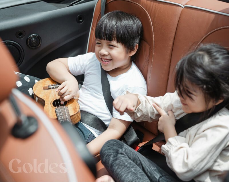Two children having fun with a Goldesi ukulele while traveling in a car. The Goldesi ukulele is portable and perfect for kids of all ages.
