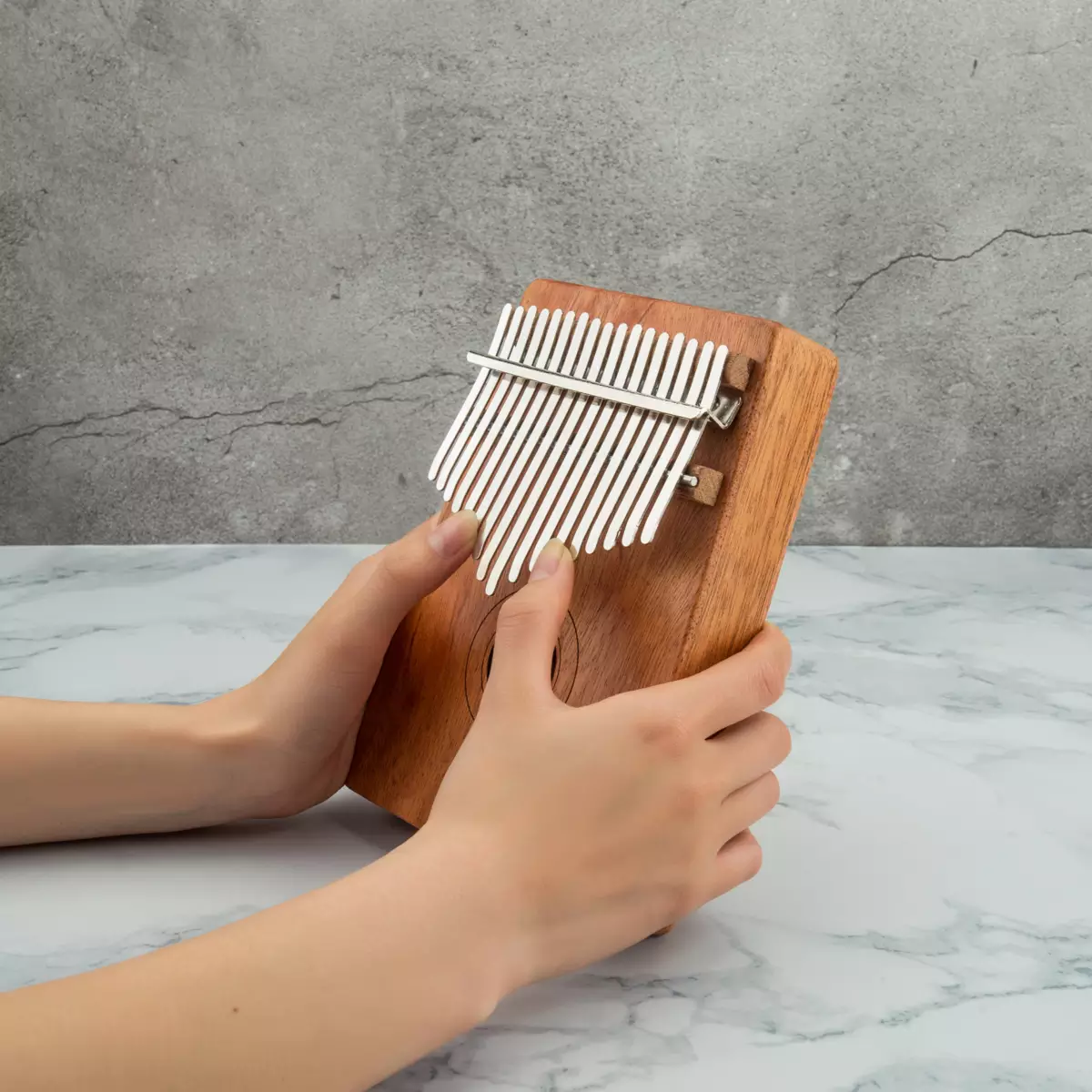 Kalimba with a natural wood finish held on a marble background