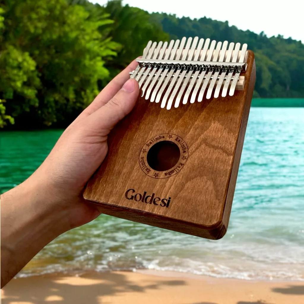 Goldesi wooden kalimba being held by a hand with a scenic nature and beach background.