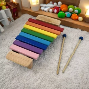 Colorful Goldesi xylophone with sticks placed on a rug next to plush toys